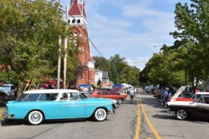Vintage car show on sunny street by brick building.